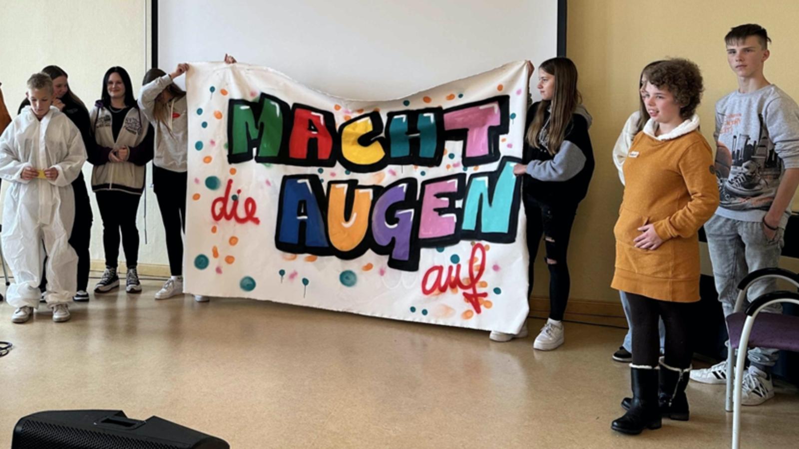 Schler*innen von Wittenberger Schulen halten ein Plakat mit dem Motto "Macht die Augen auf"